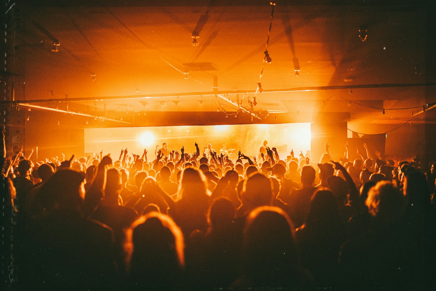Folla con le mani alzate si gode una band che si esibisce su un palco illuminato.