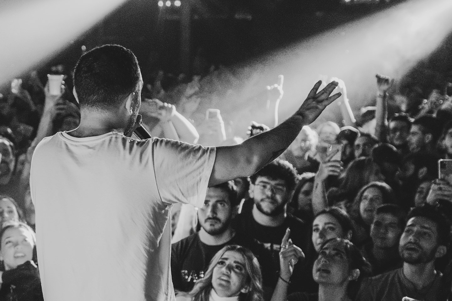 Artista sul palco con un braccio alzato davanti a una folla che applaude.