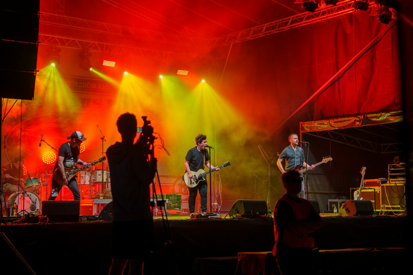 Musicisti di una rock band che suonano strumenti elettrici su un palco all'aperto.