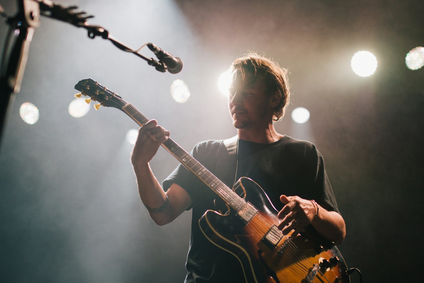Uomo che suona la chitarra elettrica su un palco fumoso.