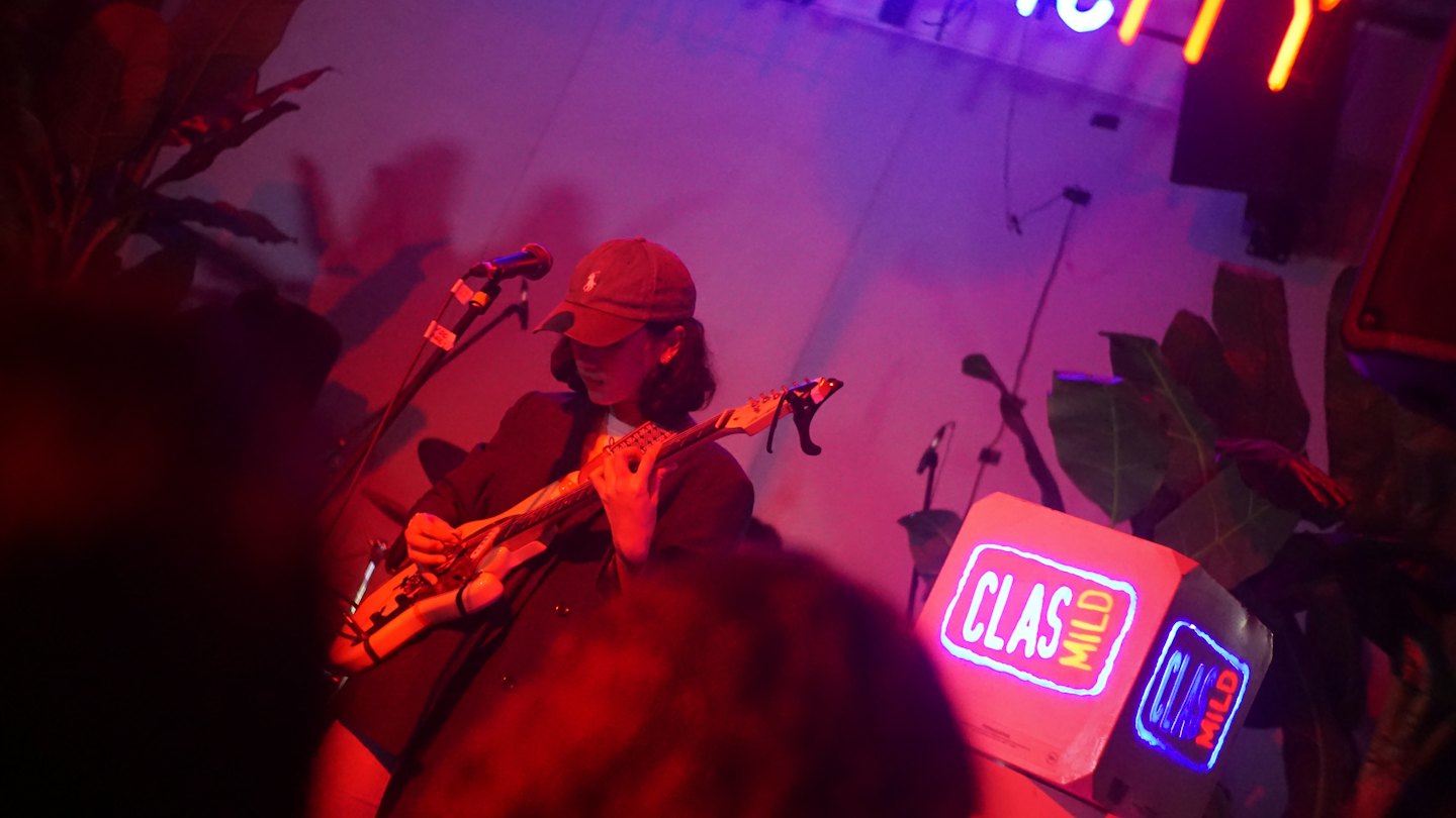 Un musicista suona la chitarra elettrica su un palco con insegne al neon.